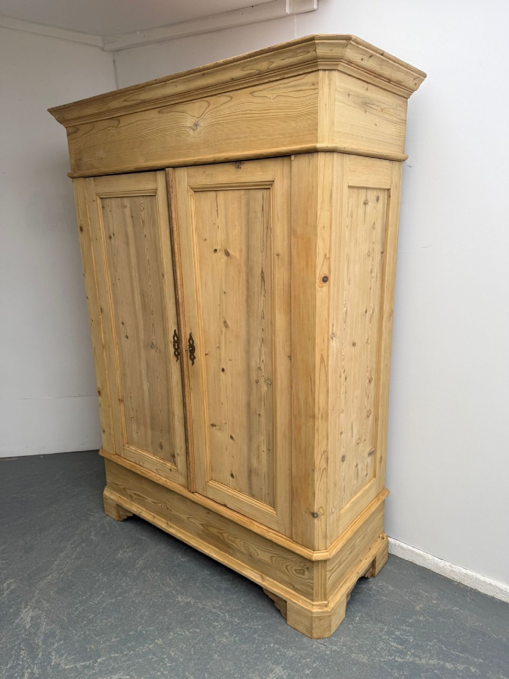 An early Georgian pine knockdown wardrobe with a prominent moulded cornice, two flat-panelled doors, and a sturdy plinth base.