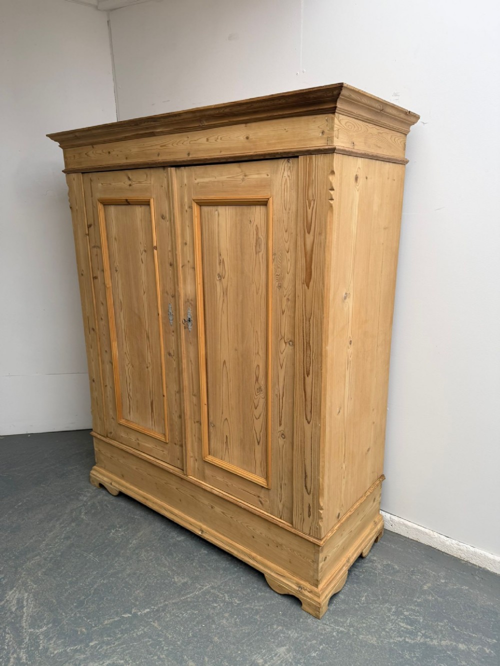 A low two-door natural pine wardrobe featuring twin moulded door panels, a prominent cornice, and a plinth base.
