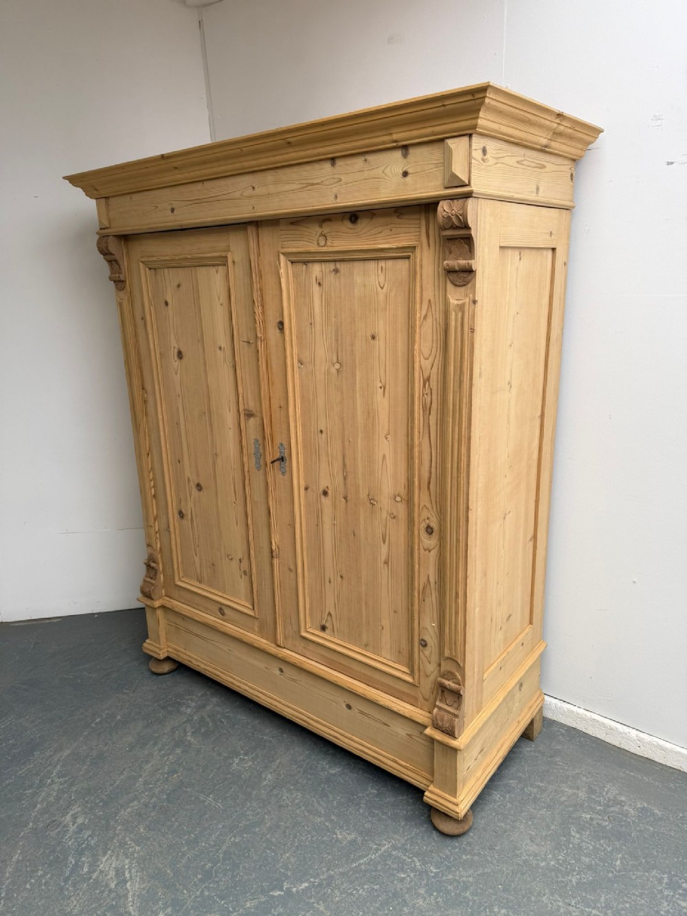 A Victorian stripped pine two-door wardrobe featuring a knockdown construction, carved corbels, panelled doors, metal escutcheons, and bun feet.