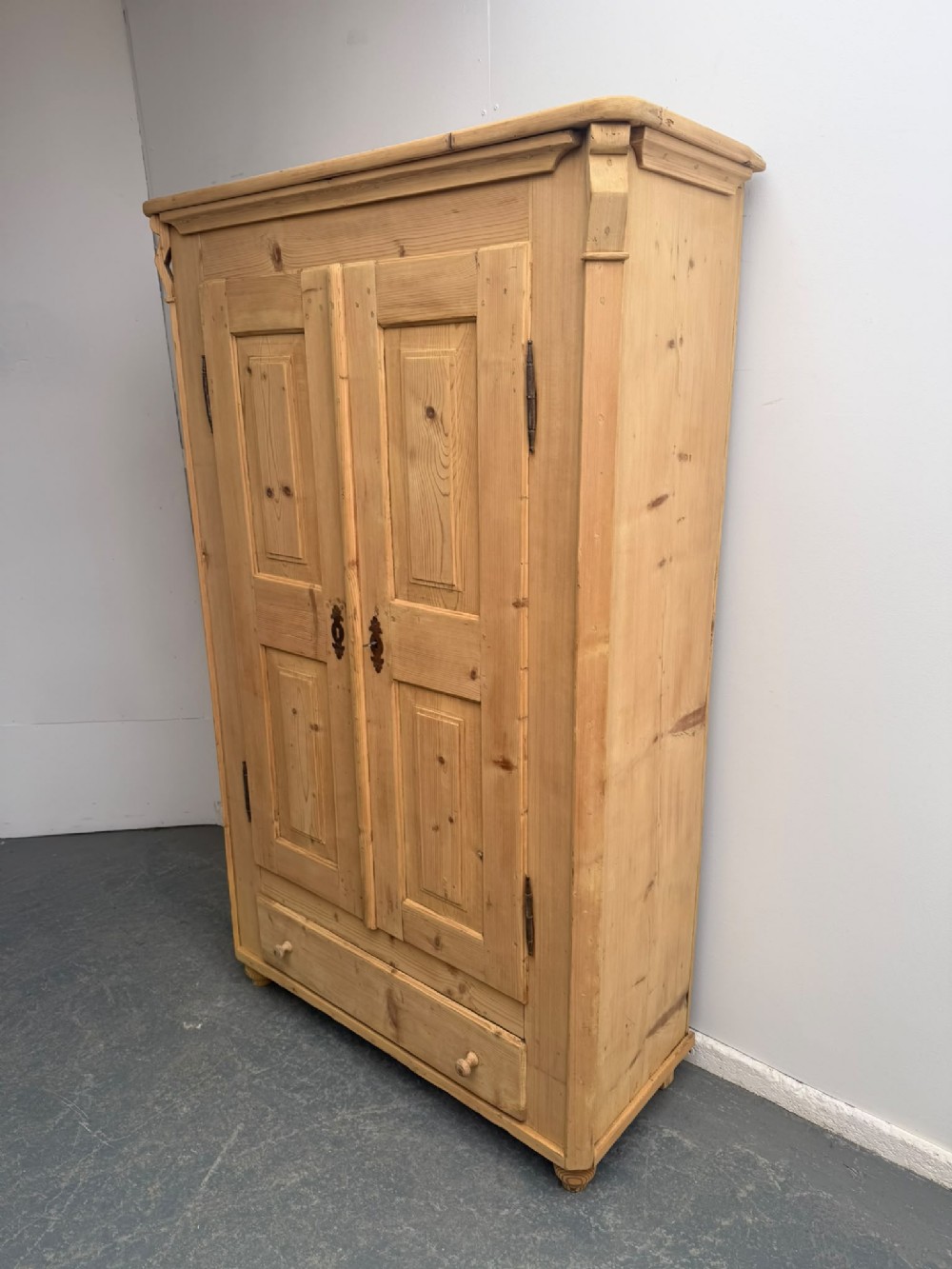 A Georgian natural stripped pine wardrobe featuring double panelled doors, iron hardware, and a lower drawer.
