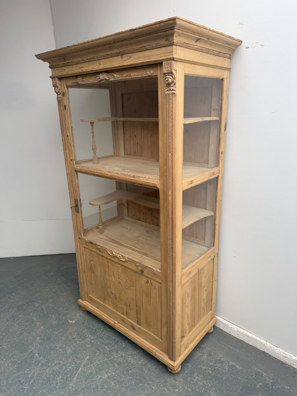 A tall Victorian stripped pine display cabinet with glass front and side panels, carved corner detail, and interior timber shelving.