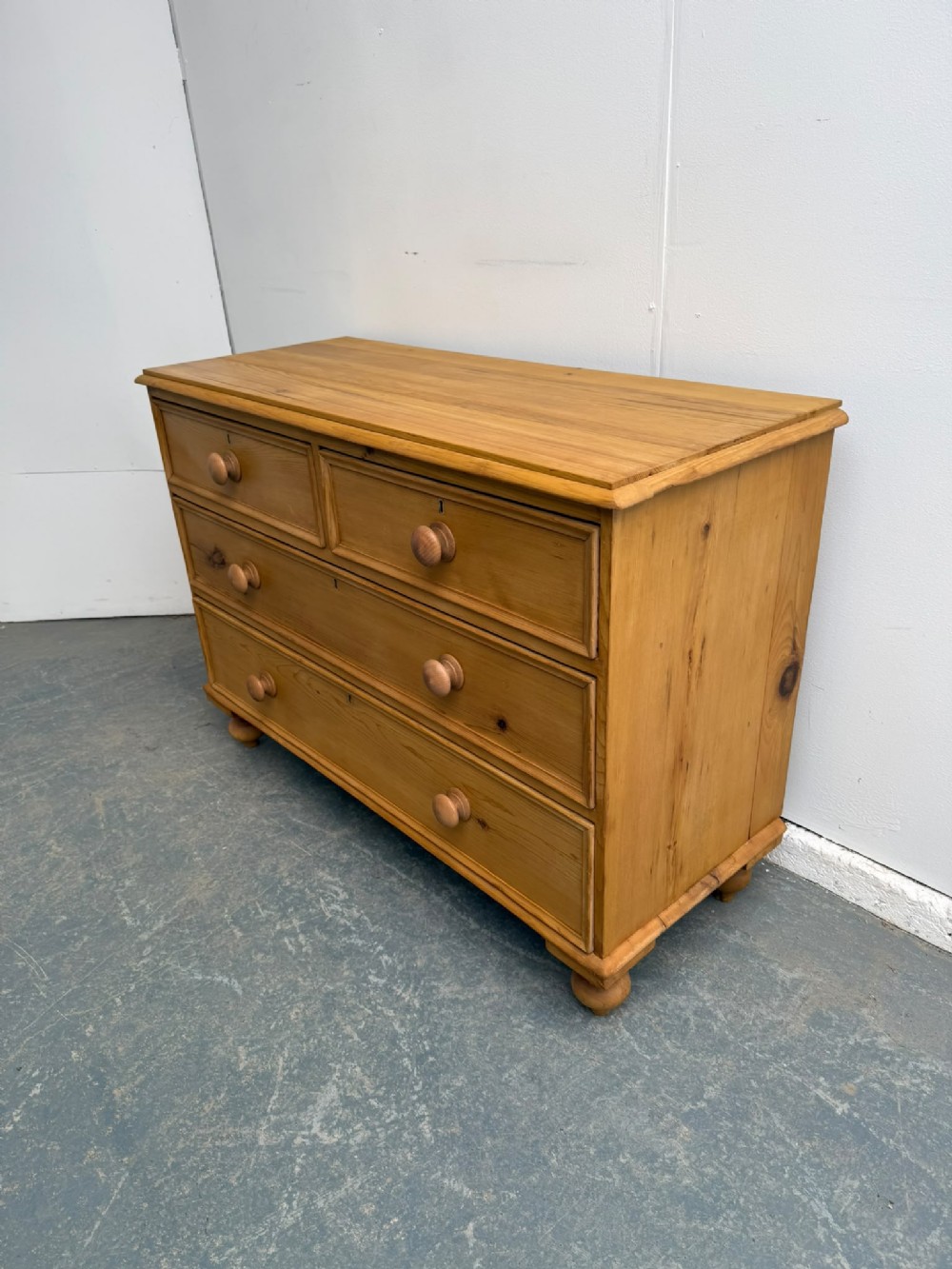 A low and wide Victorian waxed pine chest of drawers featuring two short drawers over two long drawers with turned wooden knobs and bun feet.
