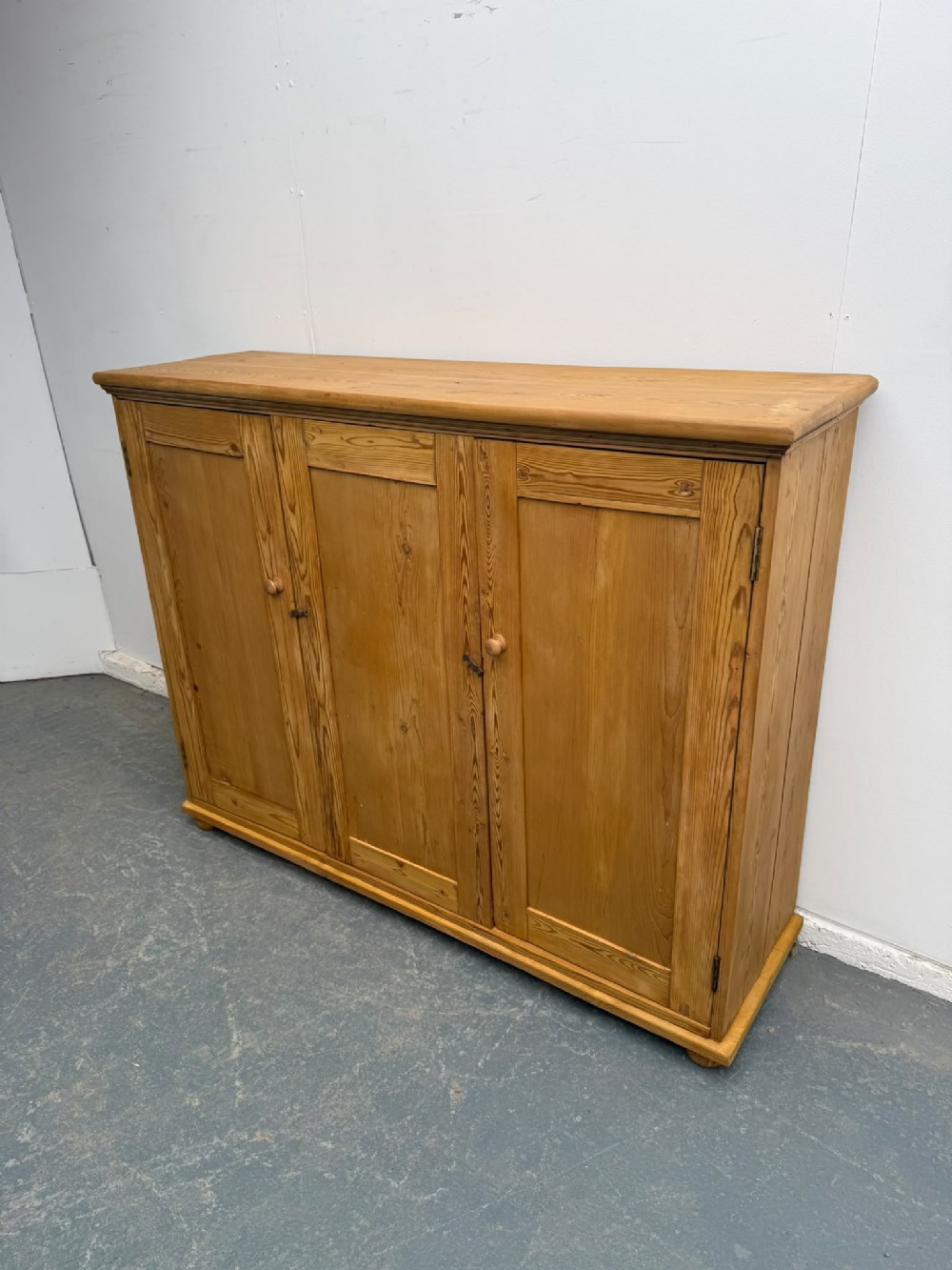 A large Victorian waxed pine storage cupboard featuring panelled doors and turned wooden knobs on a low plinth base.