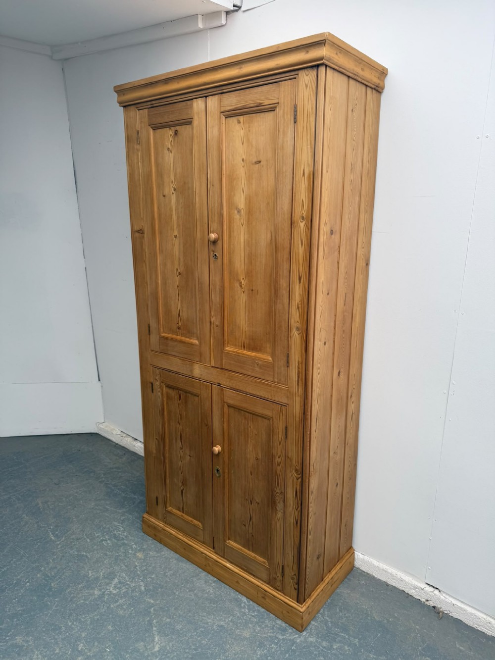 A tall Victorian pine storage cupboard with four panelled doors, wooden knobs, and a waxed finish against a white background.