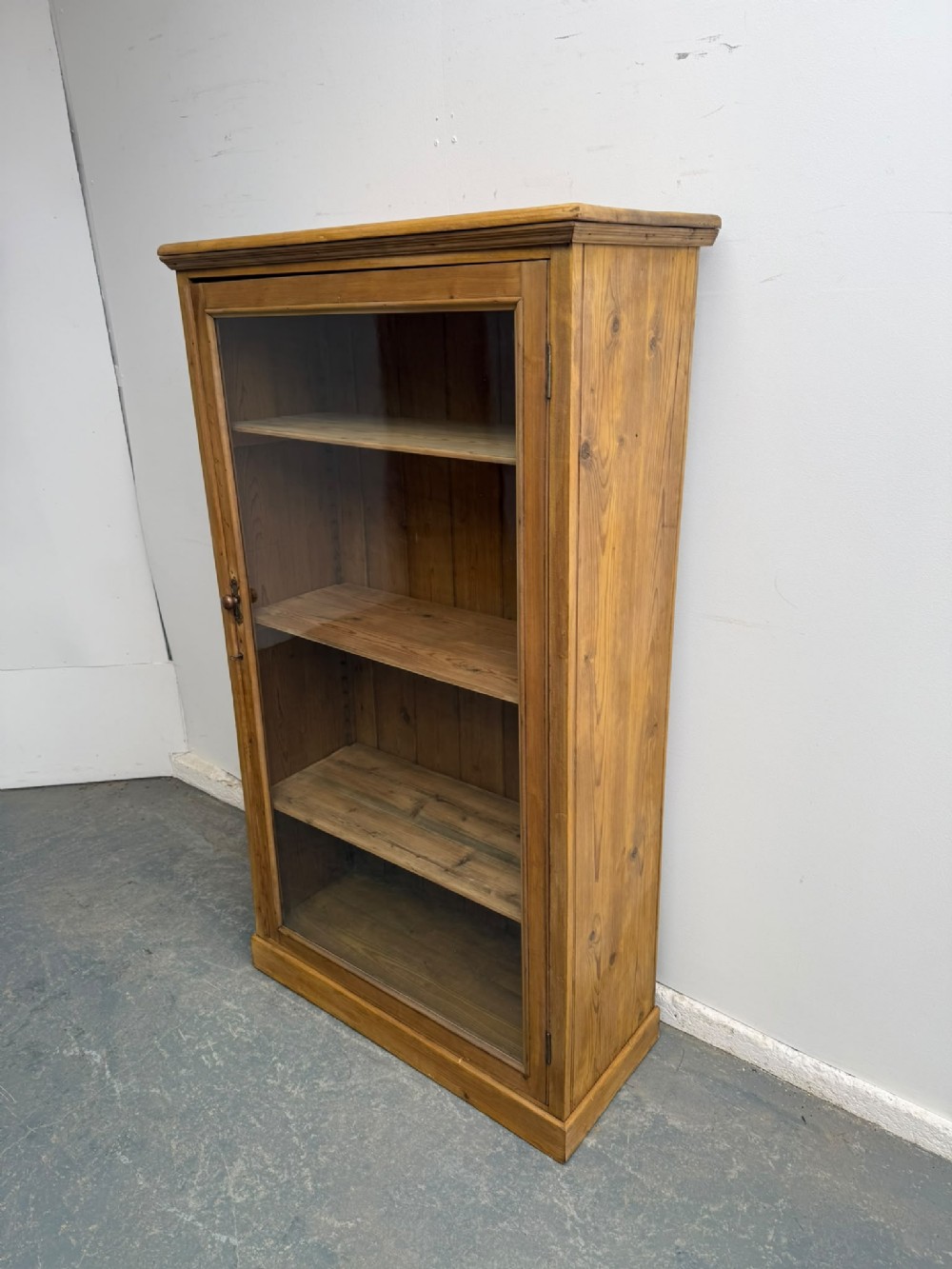 A Victorian waxed pine display cabinet featuring a single glazed door and interior adjustable wooden shelves.