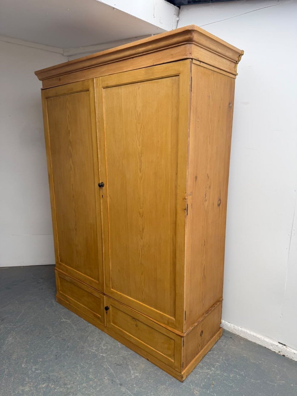 A large two-door Victorian waxed pine cupboard featuring recessed panel doors, two bottom drawers, turned wooden knobs, and a stepped top moulding.