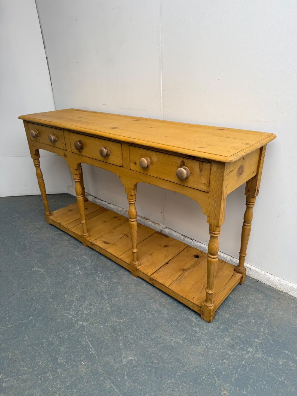 A long Georgian antique pine pot board server featuring three drawers with turned wooden handles, shaped aprons, turned legs, and an open lower shelf.