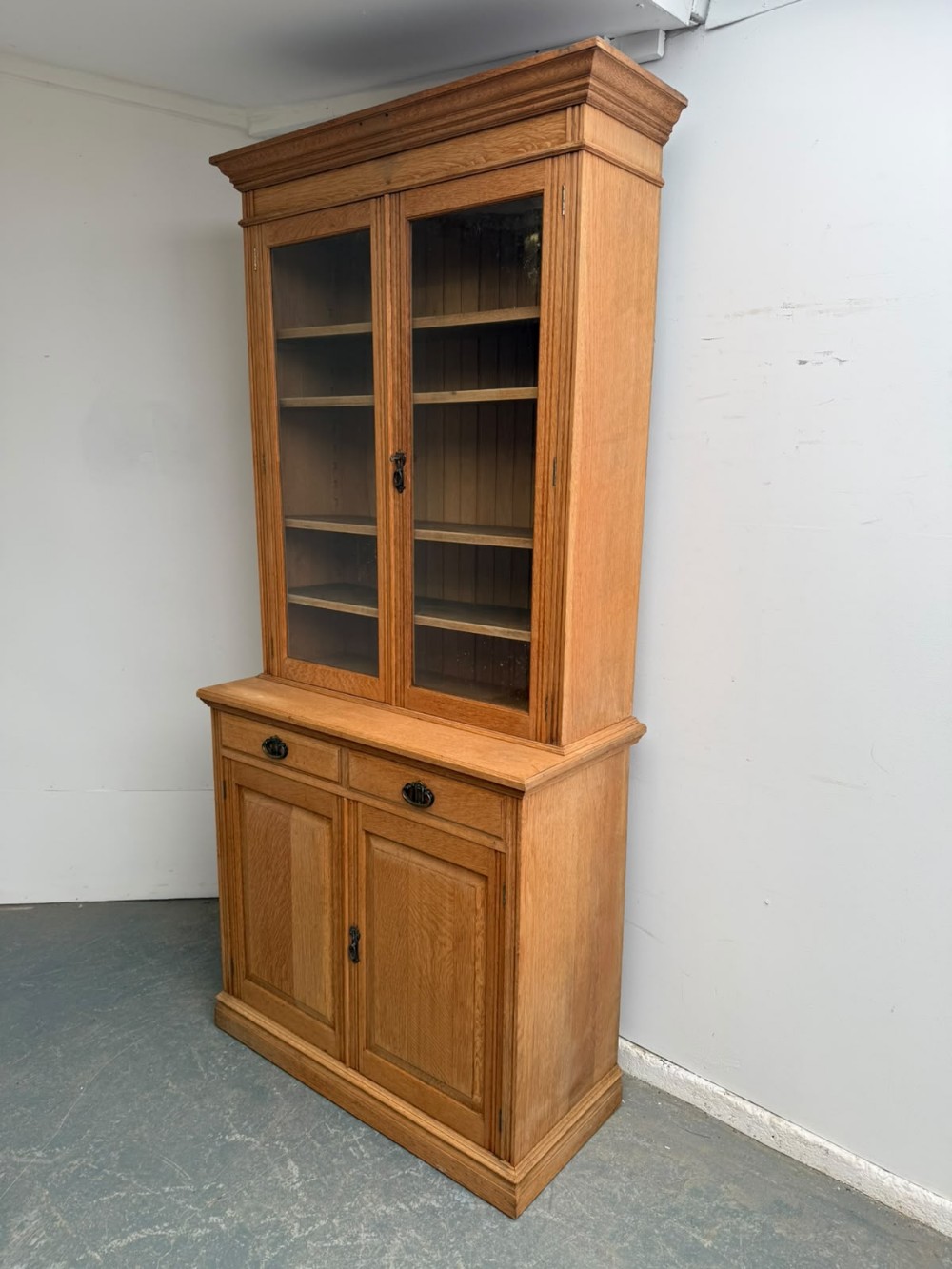 A two-piece Arts and Crafts oak cabinet with upper glazed double doors and lower panelled cupboard doors with two drawers.