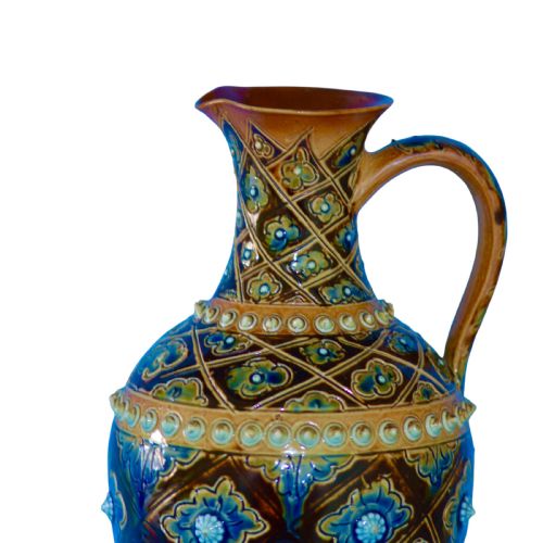 fig 1. A Victorian salt-glazed stoneware jug featuring geometric diamond relief patterns, blue glazed floral rosettes, raised beaded banding, and a single handle.