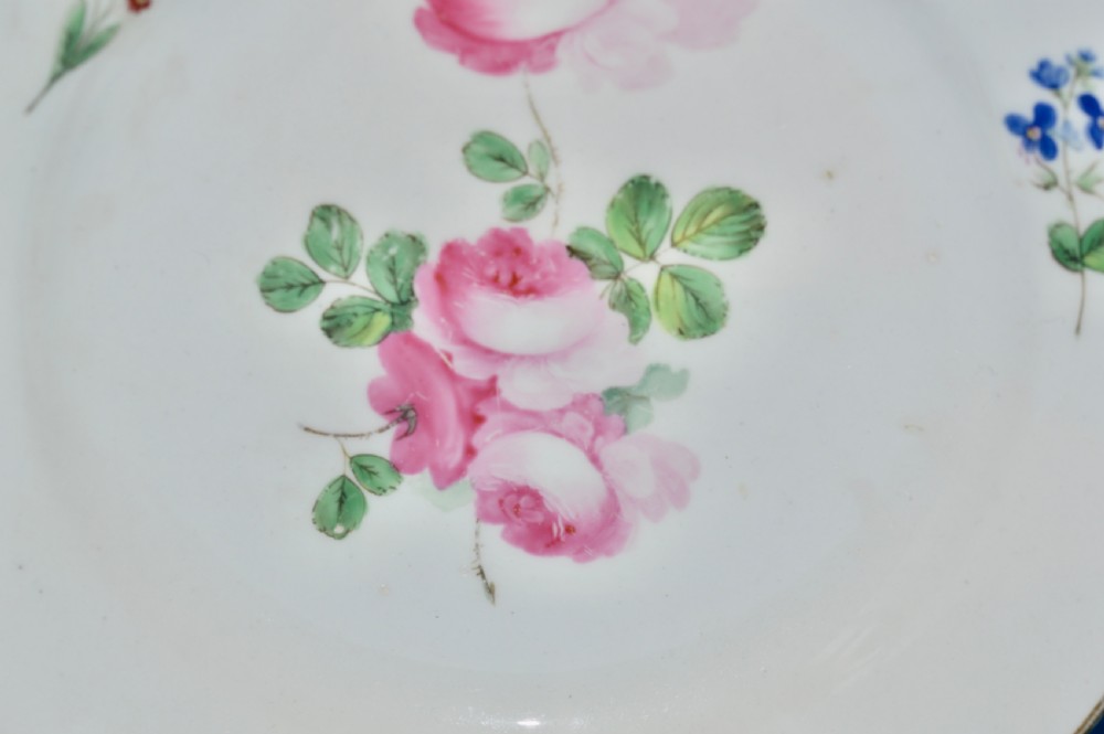 A circular white porcelain dessert plate with hand-painted pink roses at the centre, small botanical sprays along the rim, and a slender gilded border. View II