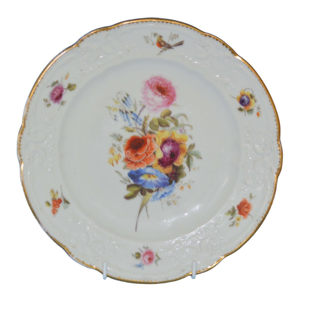 A white soft-paste porcelain plate featuring hand-painted floral motifs, a gilded scalloped rim, and a small bird accent.