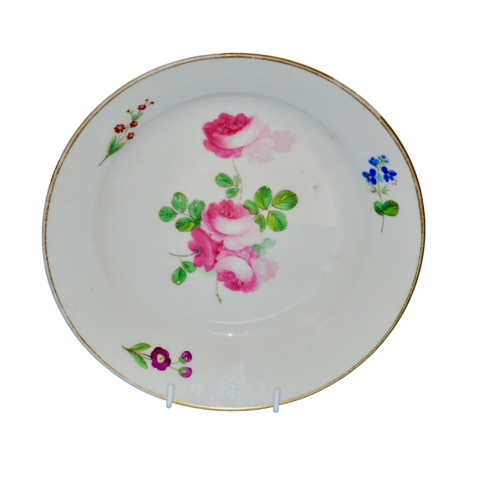 A circular white porcelain dessert plate with hand-painted pink roses at the centre, small botanical sprays along the rim, and a slender gilded border.