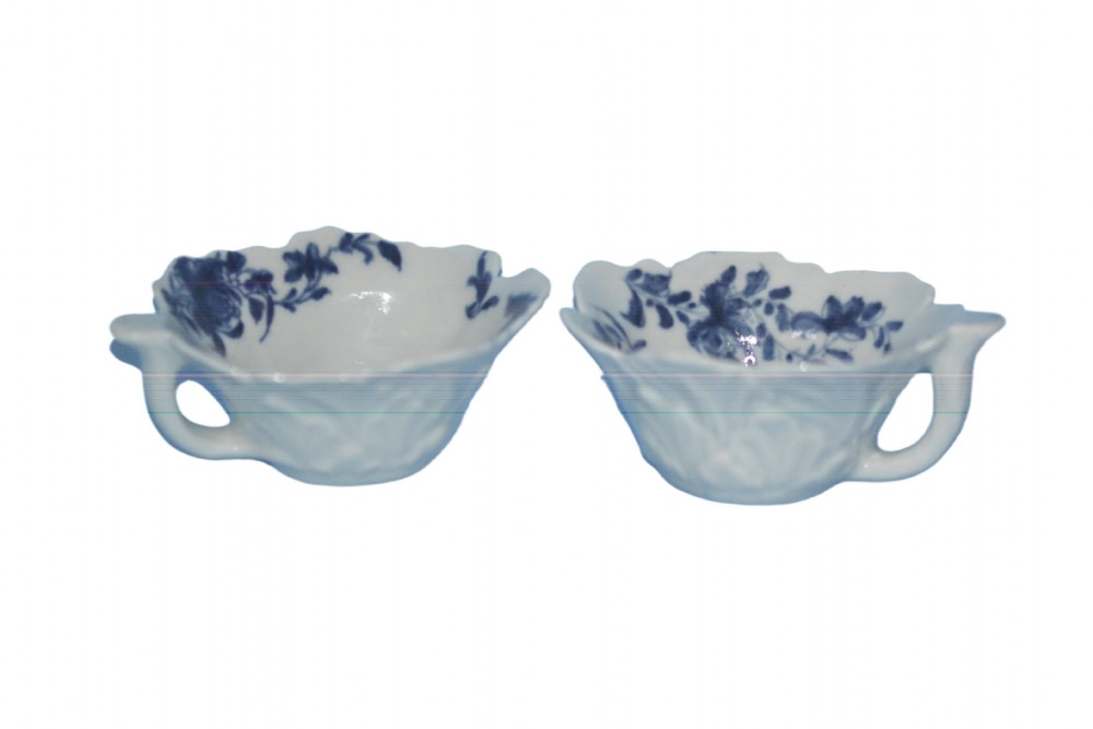 A pair of small 18th-century English soft-paste porcelain butter boats with leaf-moulded exteriors, loop handles, and blue floral underglaze painted interiors.