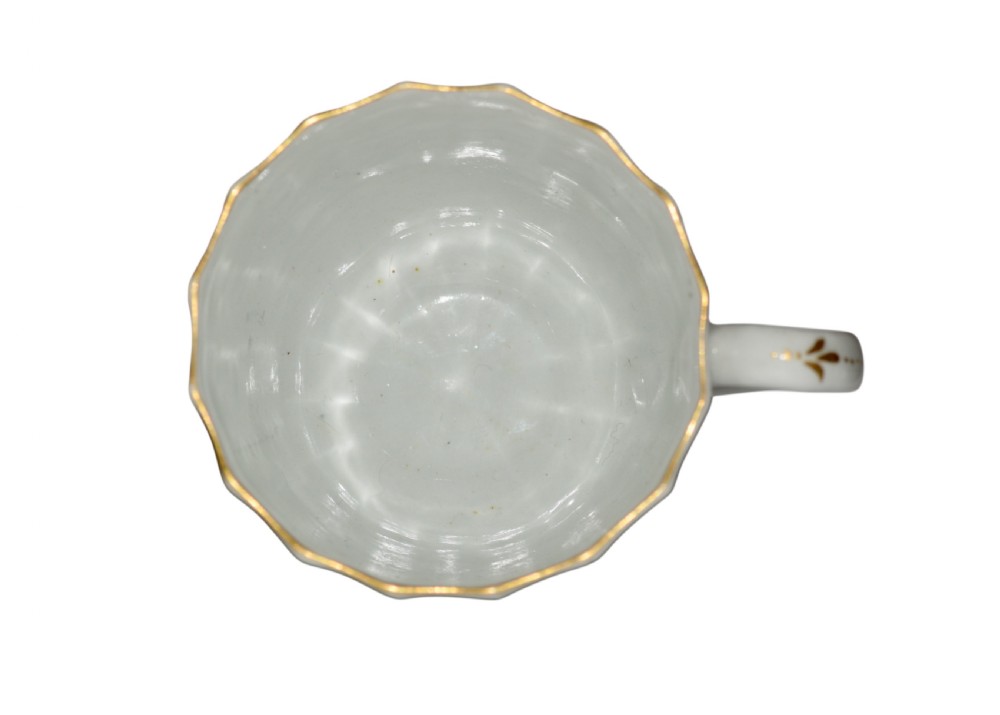 A white fluted porcelain coffee cup decorated with a purple transfer-printed scene of a seated couple in a garden setting, featuring a single loop handle and gilded rim. View IV