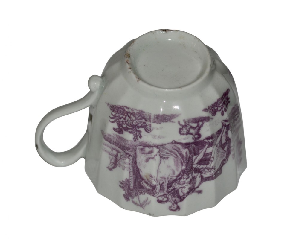 A white fluted porcelain coffee cup decorated with a purple transfer-printed scene of a seated couple in a garden setting, featuring a single loop handle and gilded rim. View VI