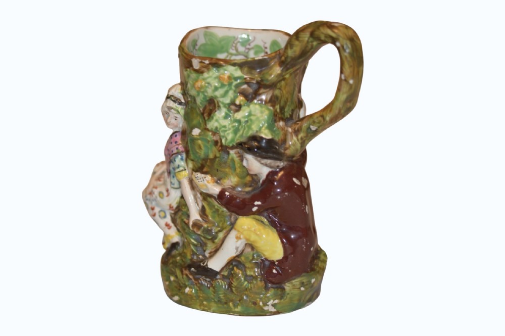 An 18th-century Staffordshire pearlware Fair Hebe jug featuring relief-moulded figures around a tree trunk with a branch-shaped handle.