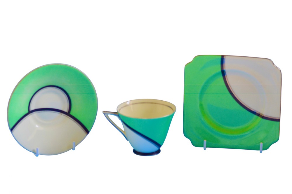 An Art Deco ceramic teacup, circular saucer, and square side plate featuring green and cream geometric panel decoration.