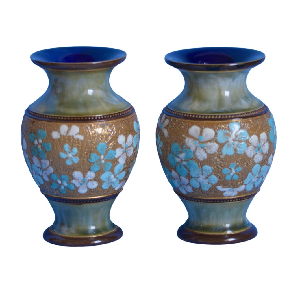 A pair of baluster-shaped Doulton Lambeth stoneware vases with textured gold-toned bodies decorated with turquoise and white floral enamel motifs below green-glazed necks.