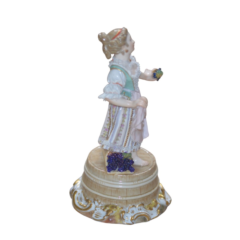 A polychrome Meissen porcelain figurine depicting a female figure holding grapes atop a circular pedestal with gilded scrollwork. View III