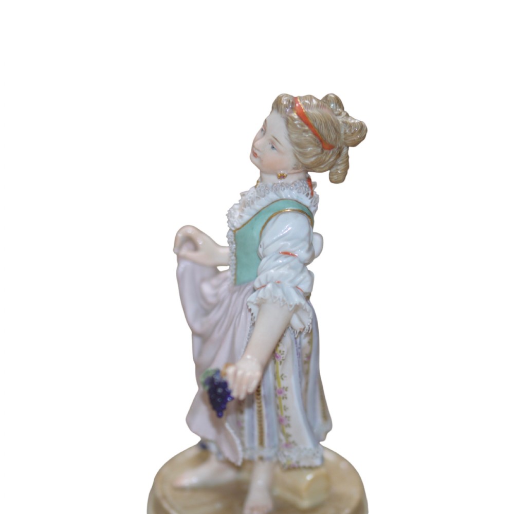 A polychrome Meissen porcelain figurine depicting a female figure holding grapes atop a circular pedestal with gilded scrollwork. View V