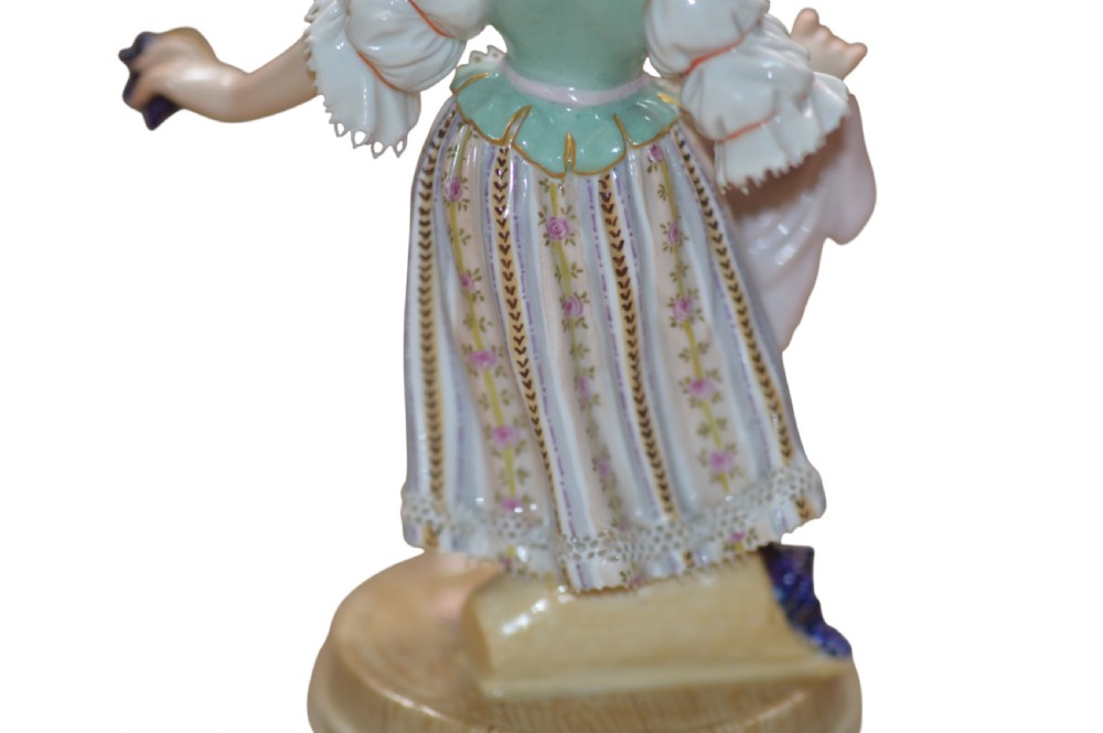 A polychrome Meissen porcelain figurine depicting a female figure holding grapes atop a circular pedestal with gilded scrollwork. View VII