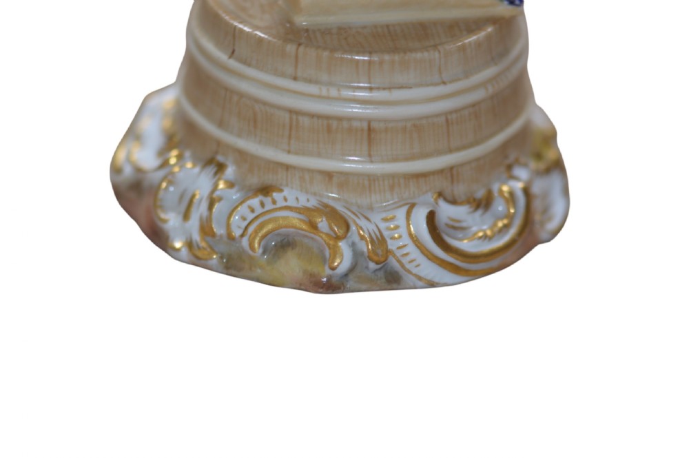 A polychrome Meissen porcelain figurine depicting a female figure holding grapes atop a circular pedestal with gilded scrollwork. View VIII