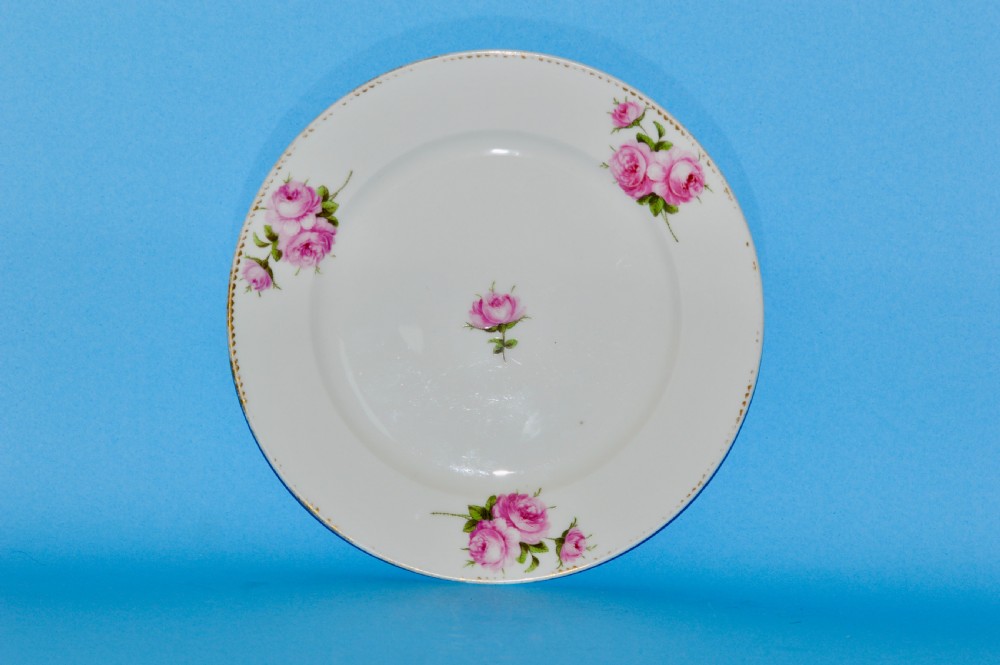 A circular white porcelain plate featuring hand-painted pink rose sprays around the border and in the centre, finished with a gilded rim.