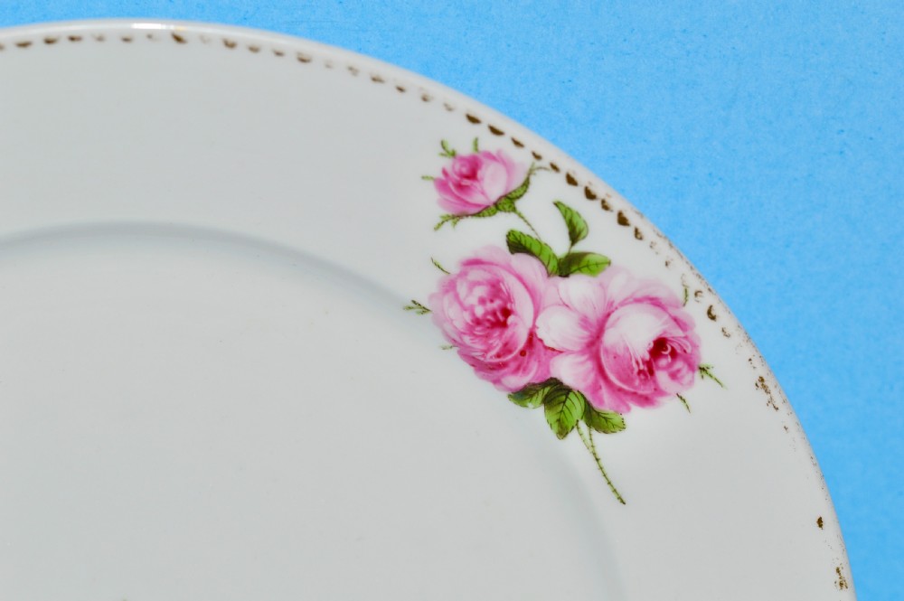 A circular white porcelain plate featuring hand-painted pink rose sprays around the border and in the centre, finished with a gilded rim. View III