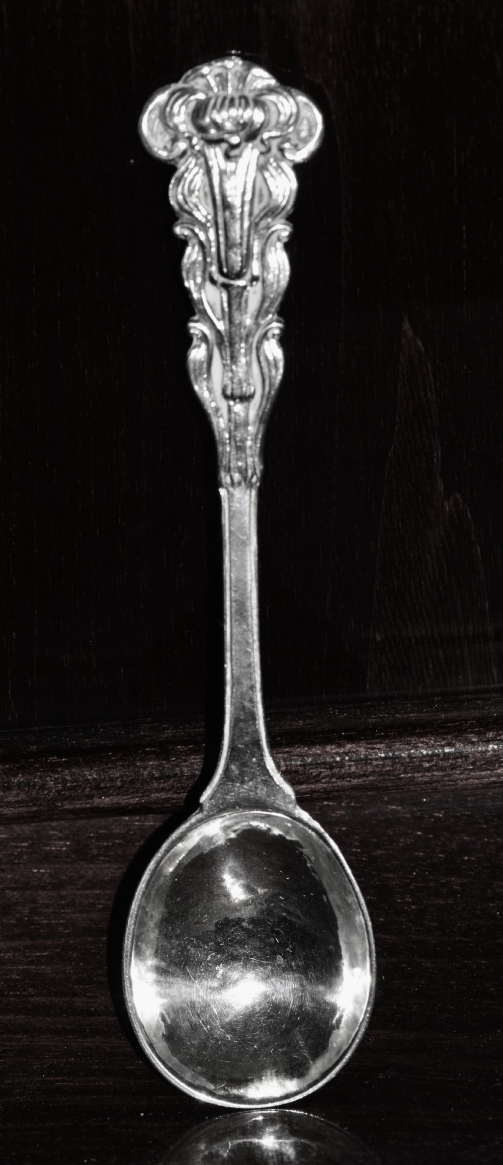 A sterling silver spoon featuring a hand-hammered bowl and an intricately carved decorative terminal with stylised floral motifs.