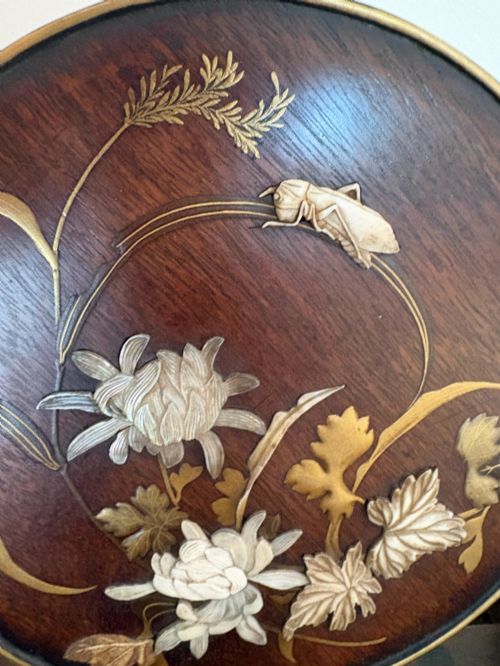fig 1. A circular dark wood Japanese table screen featuring raised mother-of-pearl floral and insect inlays, set within a carved hardwood stand.