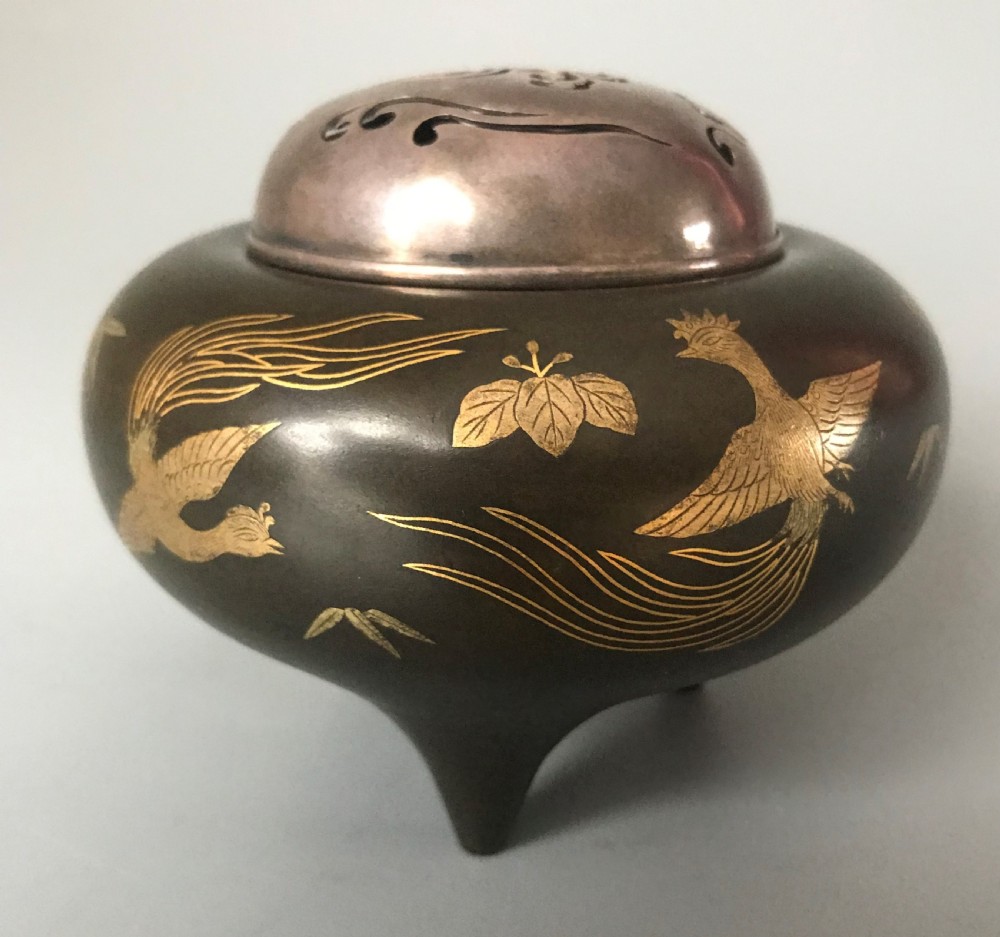 A tripod dark bronze incense burner featuring gold inlaid phoenix bird motifs and a pierced silver lid.