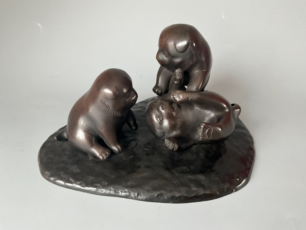 A dark brown patinated bronze Japanese okimono sculpture depicting three playful puppies on a textured base.