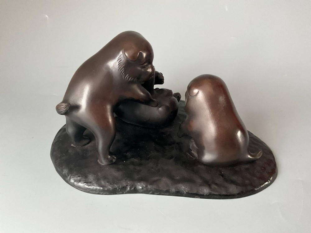 A dark brown patinated bronze Japanese okimono sculpture depicting three playful puppies on a textured base. View III