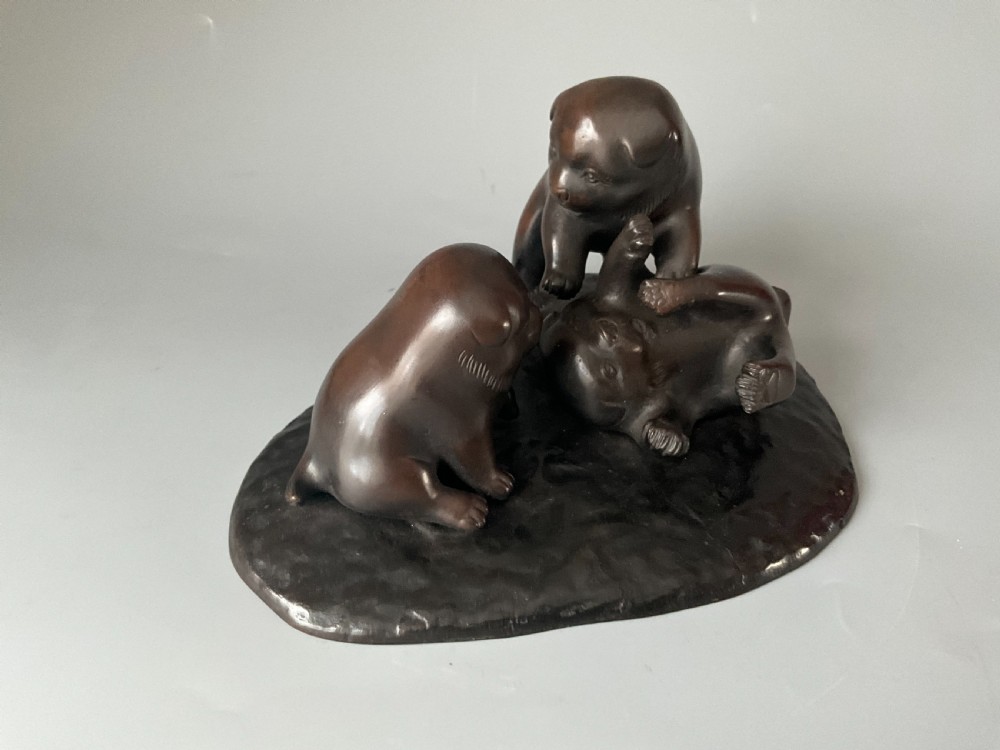 A dark brown patinated bronze Japanese okimono sculpture depicting three playful puppies on a textured base. View V