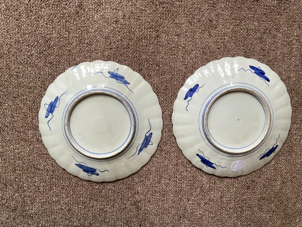 A pair of circular Japanese Imari porcelain plates featuring scalloped rims, cobalt blue and iron-red panelled borders, and central floral urn motifs. View II