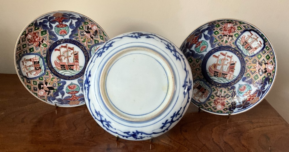 A trio of circular Japanese Imari porcelain plates featuring hand-painted European ships, figures, and geometric patterns in cobalt blue, iron red, green, and gold. View II