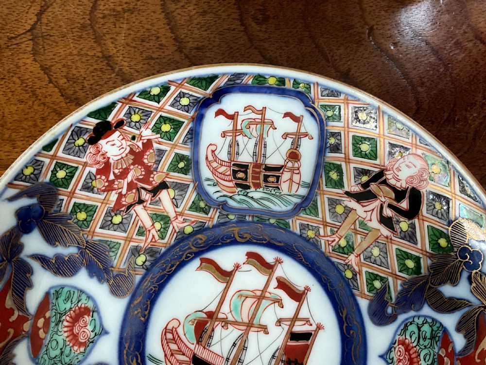 A trio of circular Japanese Imari porcelain plates featuring hand-painted European ships, figures, and geometric patterns in cobalt blue, iron red, green, and gold. View IV