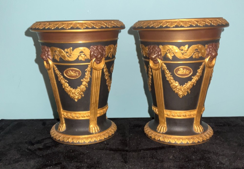 A pair of antique black basalt vases featuring gilt and bronzed neoclassical relief decorations, including lion masks and swags.