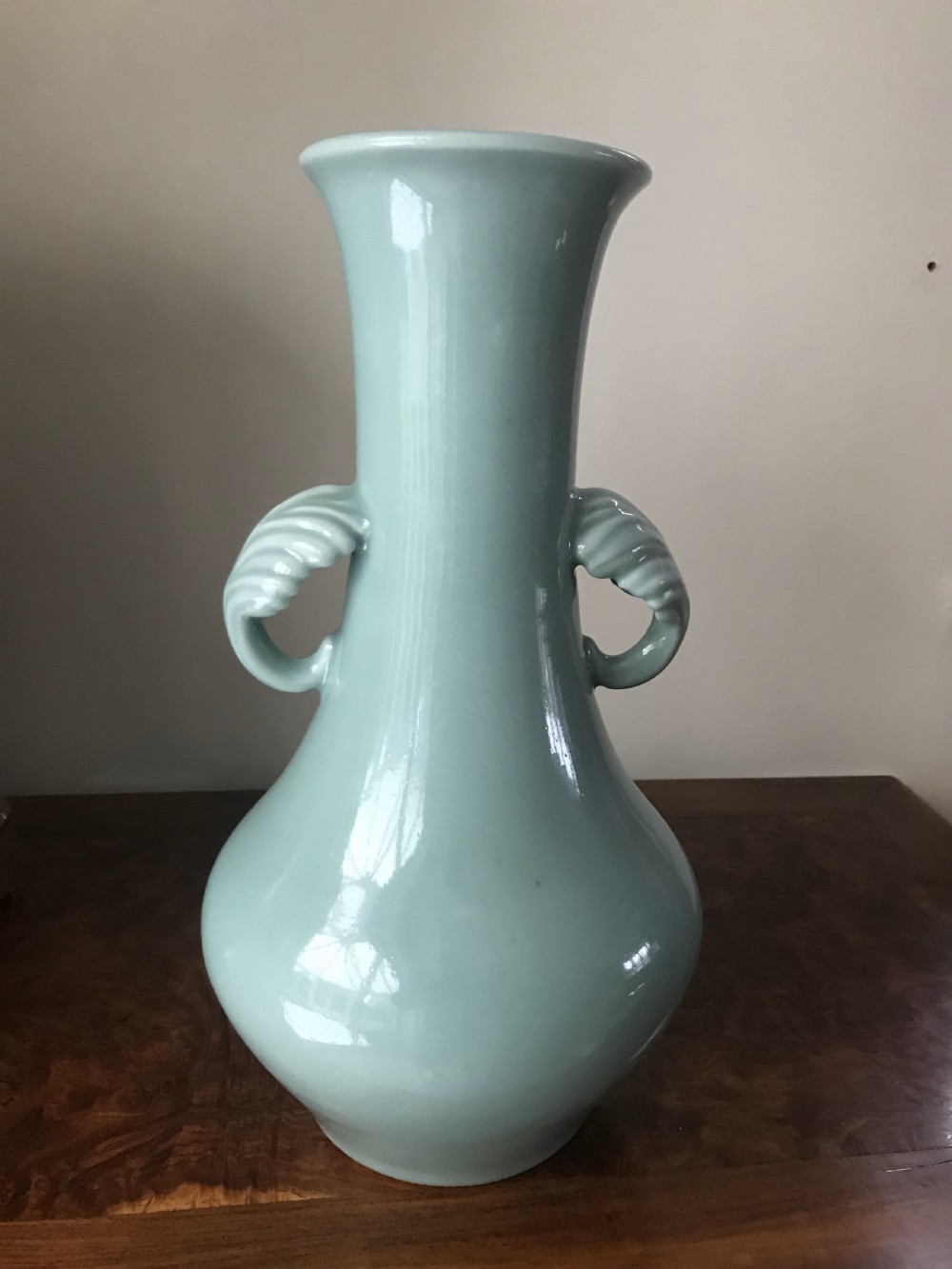 A tall pale green celadon porcelain vase featuring twin shell-shaped handles, a slender flared neck, and a bulbous lower body.
