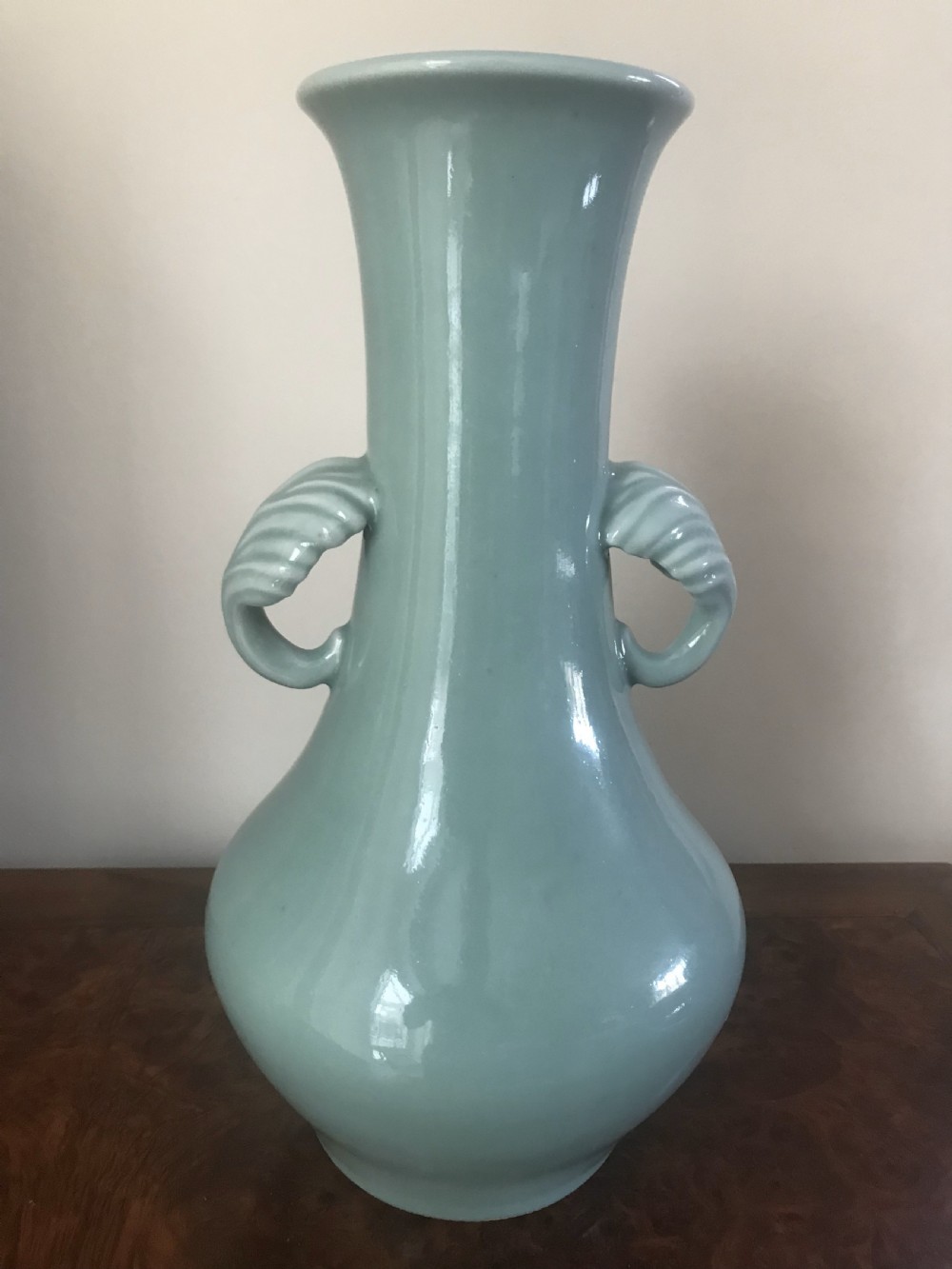A tall pale green celadon porcelain vase featuring twin shell-shaped handles, a slender flared neck, and a bulbous lower body. View II