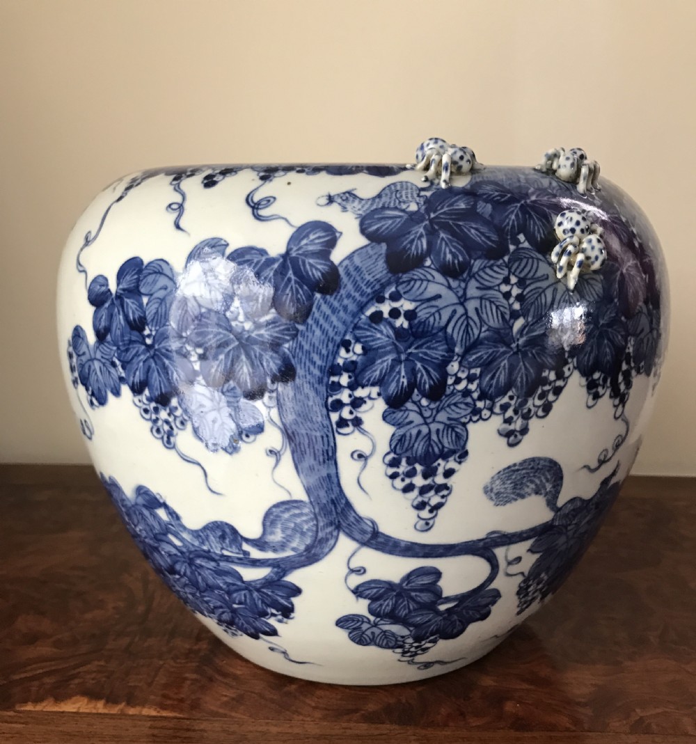 A rounded blue and white Japanese porcelain vase decorated with grapevine motifs and small three-dimensional relief creatures near the rim.