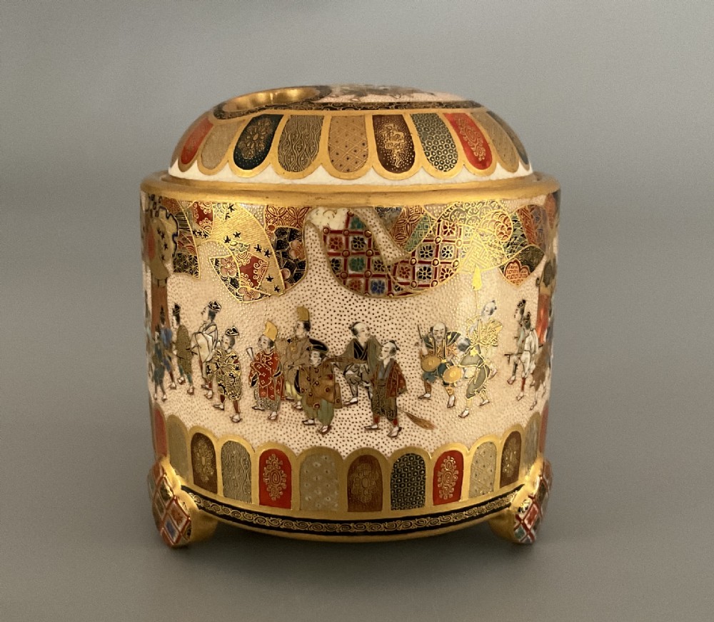 A cylindrical cream earthenware Satsuma incense burner decorated with hand-painted figures in a procession, framed by geometric lappet borders and gold detailing. View IV