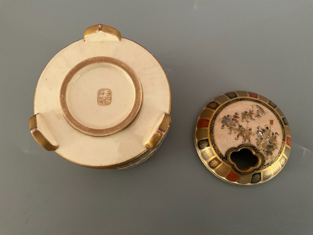 A cylindrical cream earthenware Satsuma incense burner decorated with hand-painted figures in a procession, framed by geometric lappet borders and gold detailing. View V