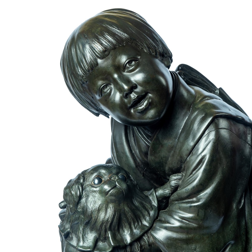 A dark patinated bronze okimono sculpture depicting a kneeling Japanese child in a kimono holding a small Pekingese dog on a rounded base. View II
