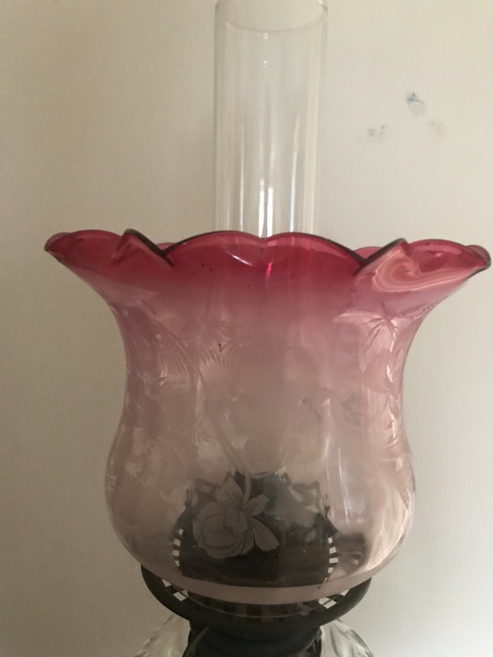 An antique Victorian glass oil lamp featuring a clear fluted crystal stem, rounded glass reservoir, central brass burner, and a tulip shade with a frilled ruby-red rim. View IV