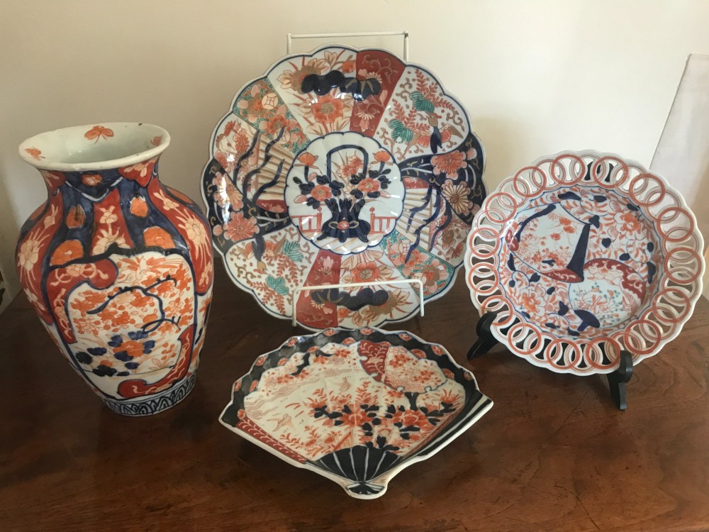 A four-piece collection of Japanese Imari porcelain comprising a baluster vase, a large scalloped charger, a fan-shaped dish, and a reticulated rim plate decorated in cobalt blue and iron red floral motifs.