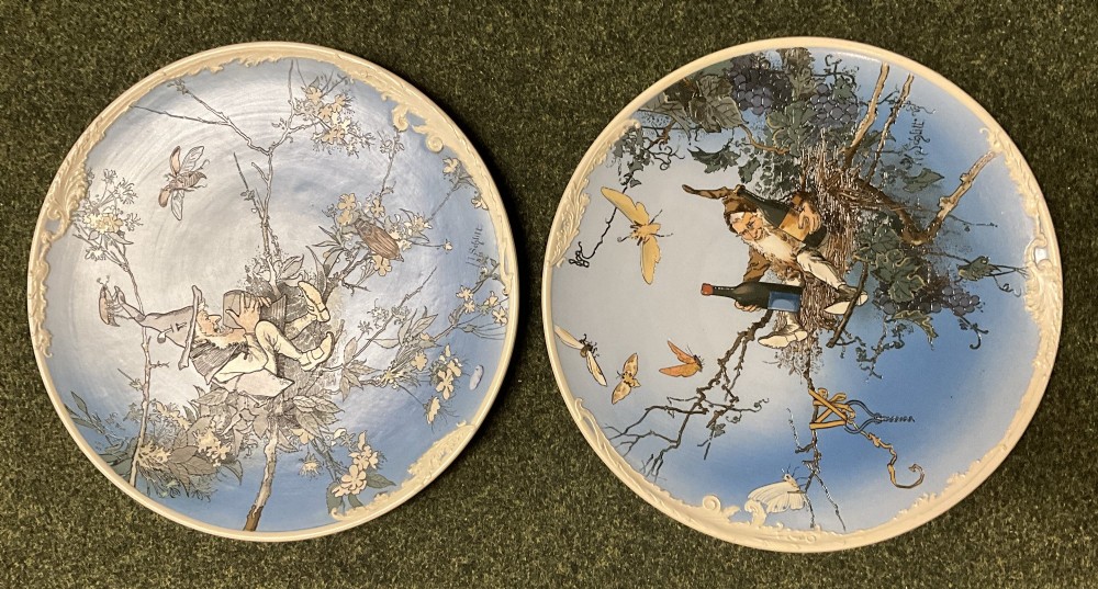 A pair of circular sky blue and cream ceramic wall plaques decorated with illustrations of gnomes and foliage.