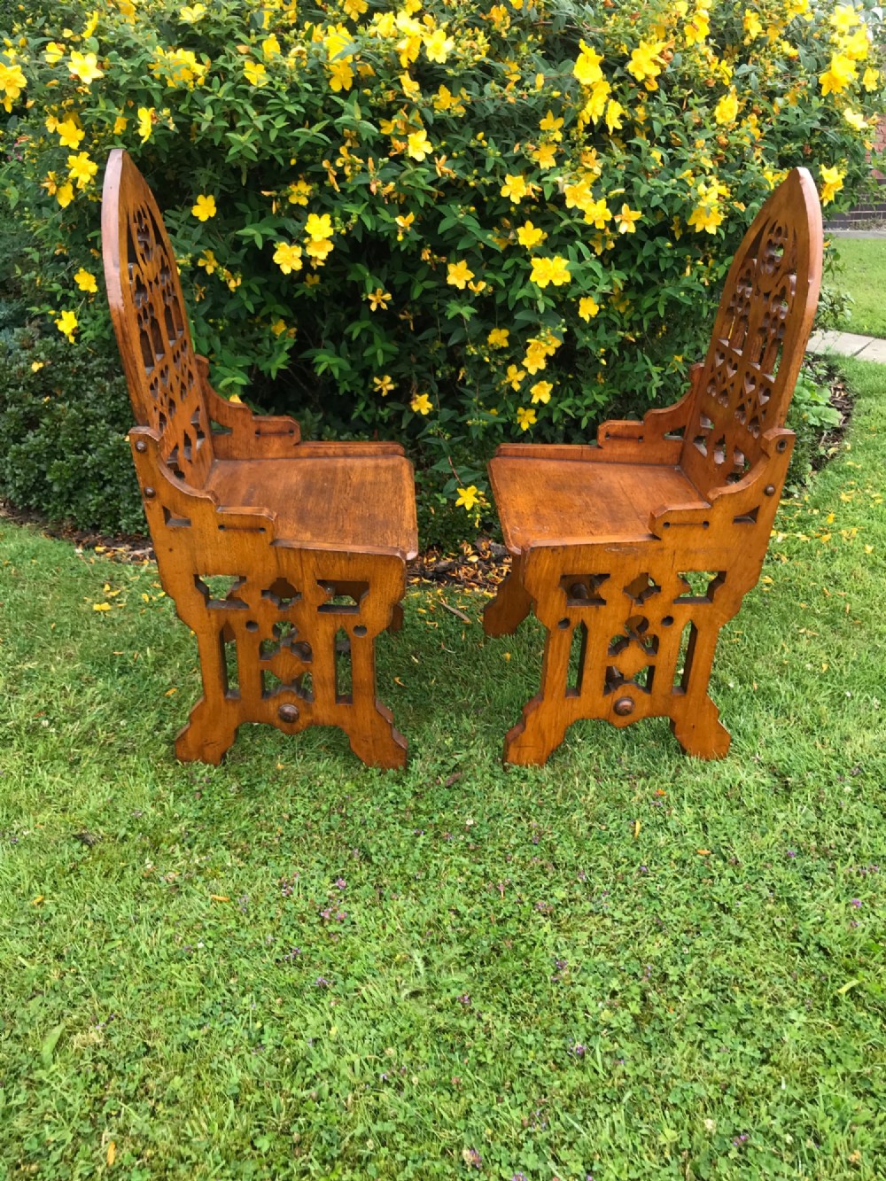 A pair of carved oak Gothic Revival hall chairs featuring pointed arch backs with tracery cut-outs and solid wooden seats. View II