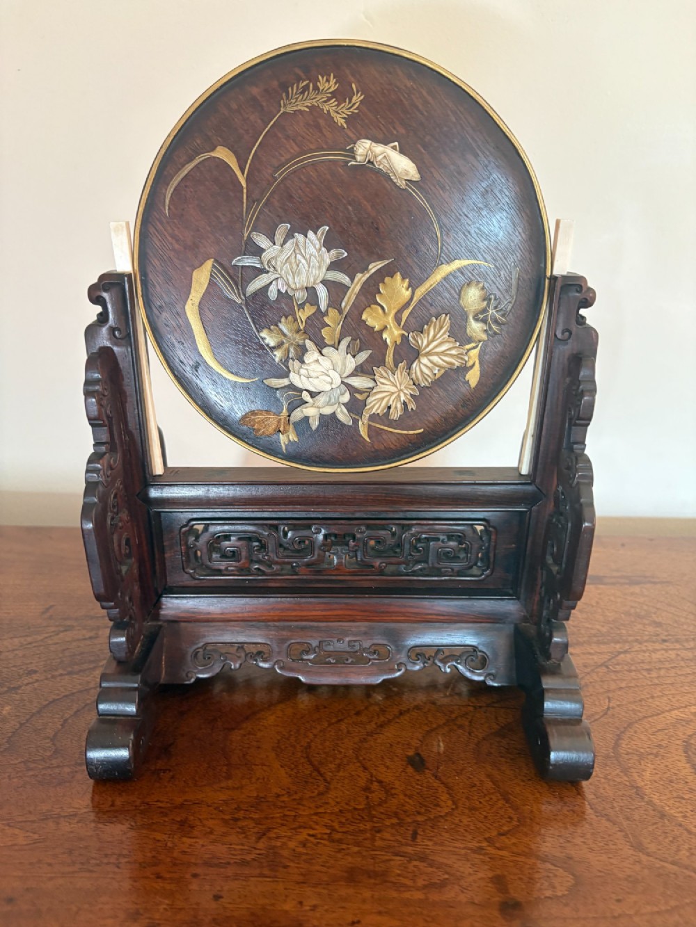 A circular dark wood Japanese table screen featuring raised mother-of-pearl floral and insect inlays, set within a carved hardwood stand.
