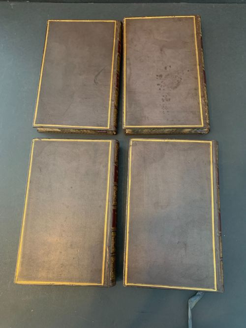 fig 1. A set of four early 19th-century leather-bound books featuring gilt tooling and titles along their dark reddish-brown spines.